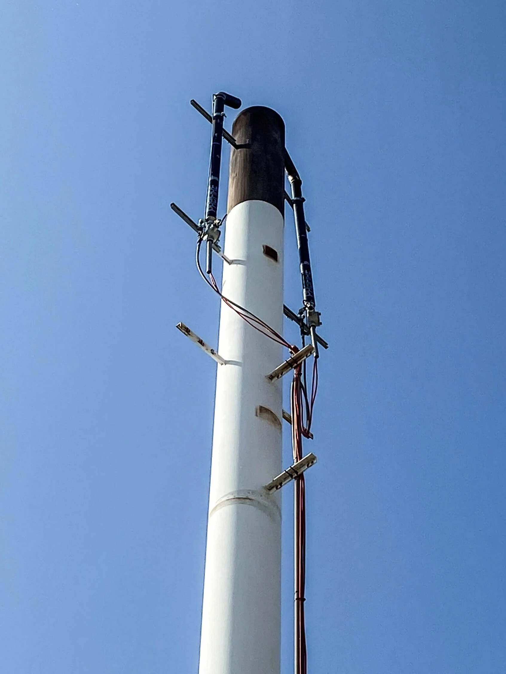 Industrial flare stack top with ignition rods and sensors installed against a clear blue sky