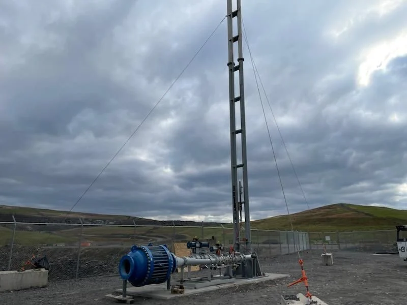 Landfill gas flare installation with blue blower, piping, and tall flare stack under cloudy skies