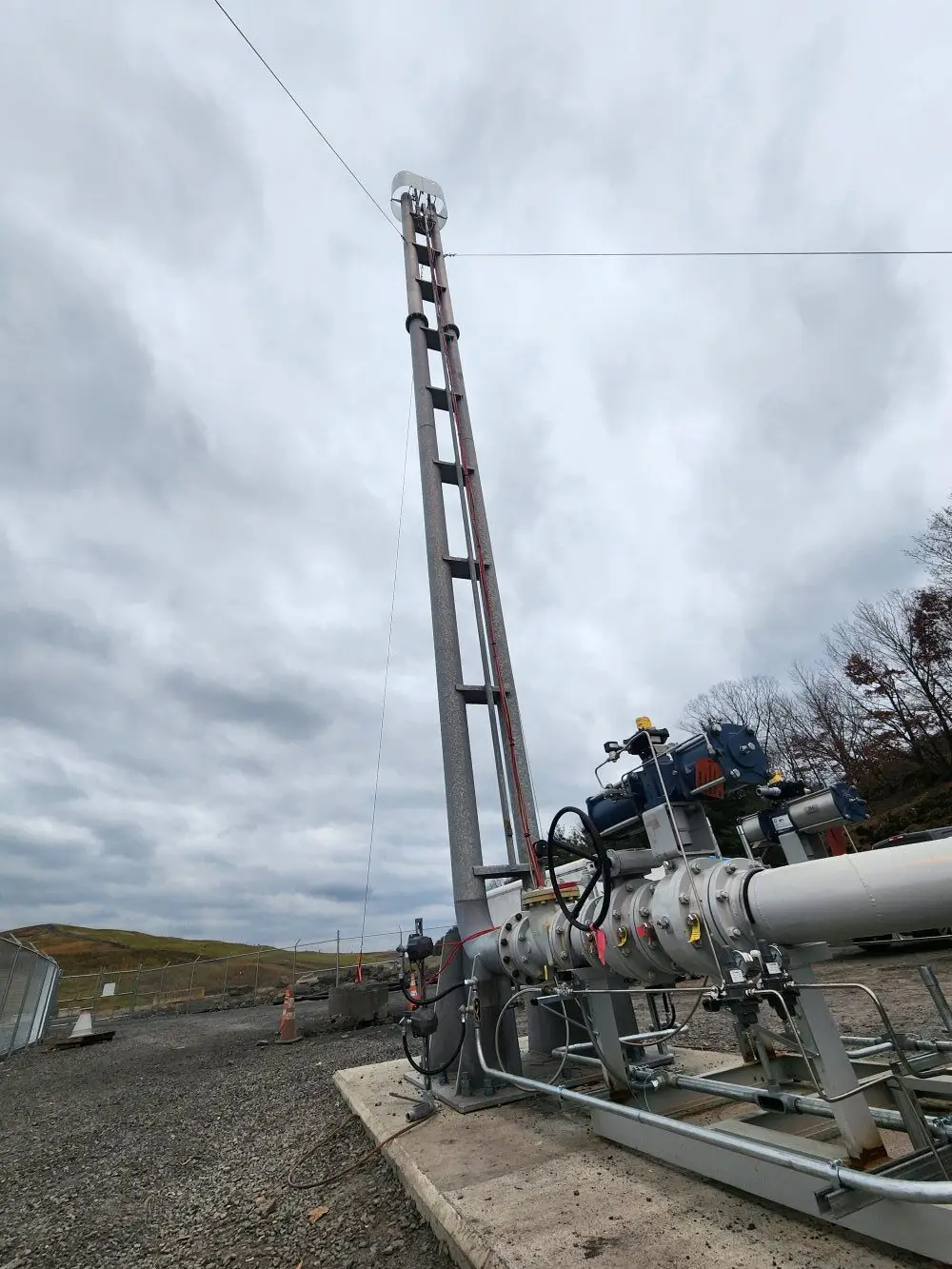 A dual candlestick flare piping and fuel train extends on the right of the image up the middle. The sky around the flare is grey and cloudy.