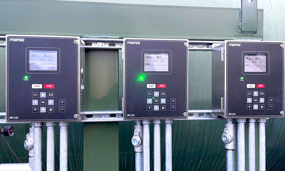 Three Profire PF2200 burner management controllers mounted side-by-side on a green panel with conduit below.
