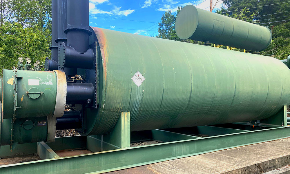 Wide view of the green horizontal thermal unit with black exhaust stacks and surrounding piping installed outdoors.