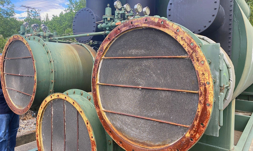 Front view of large screened inlet/outlet openings with heavily rusted flange rings and gauge tubing on the green ductwork.