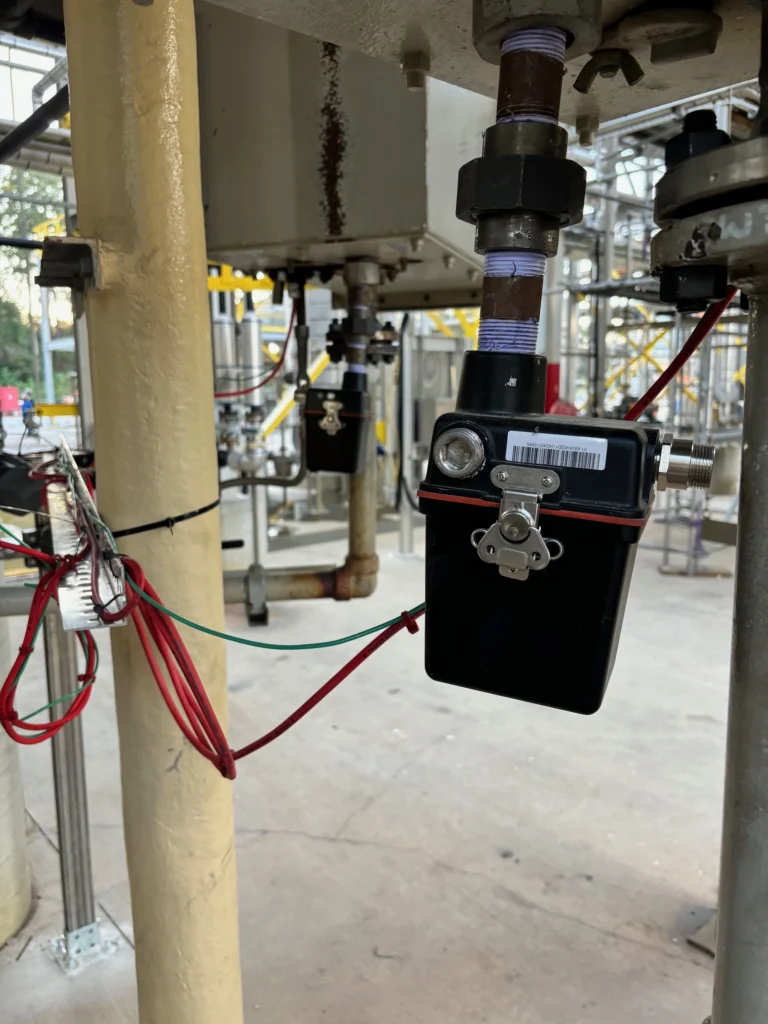 Close-up of a Fireye flame scanner mounted to burner piping with red and green field wiring in an industrial plant setting.