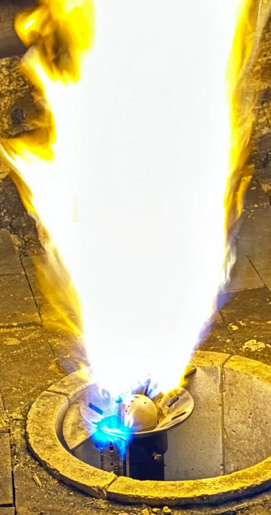 Close-up of a burner flame rising from a circular burner head inside a refractory-lined chamber, illustrating flame rod ignition or flame presence at the burner.
