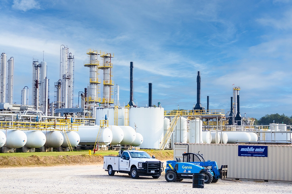 Industrial plant with storage tanks, distillation towers, piping, and service vehicles under a blue sky.
