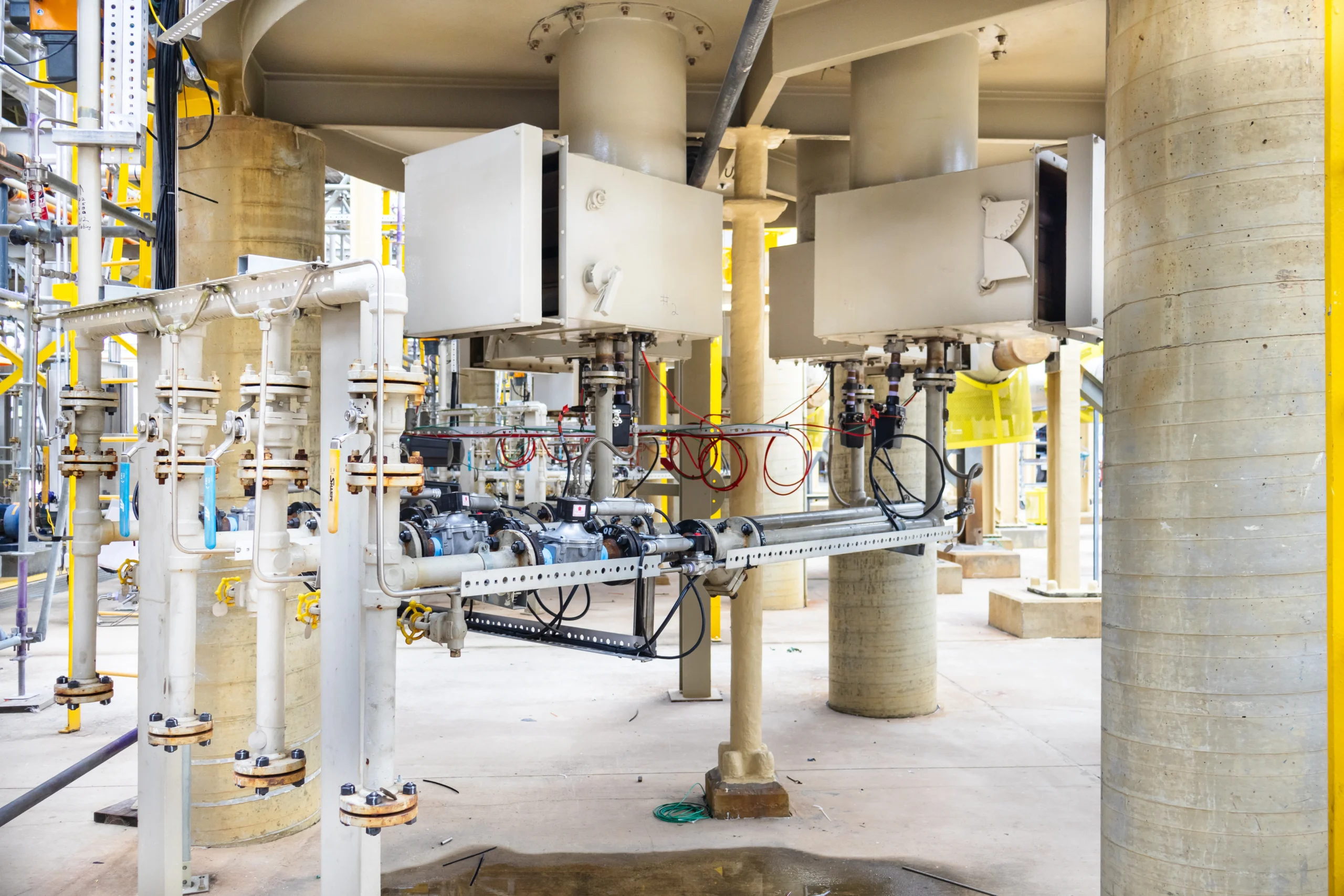 Underside view of an industrial process heater showing burner assemblies, fuel gas piping, blue-handled shutoff valves, wiring, and structural supports.