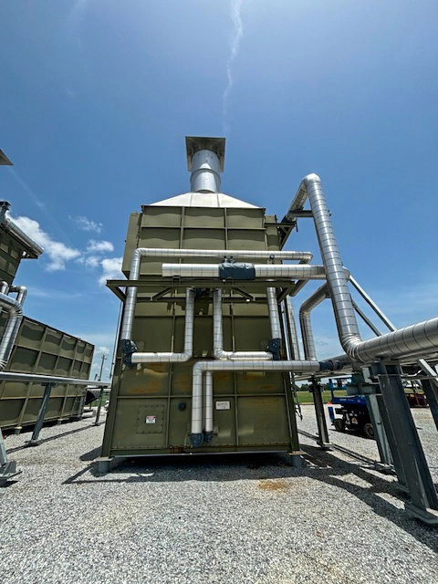 Rear view of a large outdoor industrial unit with multiple insulated ducts and pipes routed across the back and up to a vertical exhaust stack.