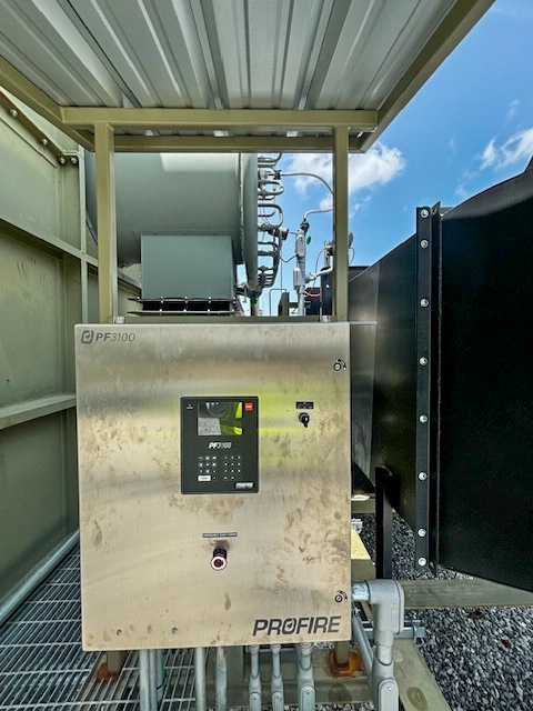 Stainless-steel Profire PF3100 control cabinet mounted outdoors beside industrial equipment, with display, keypad, and emergency stop visible on the enclosure door.