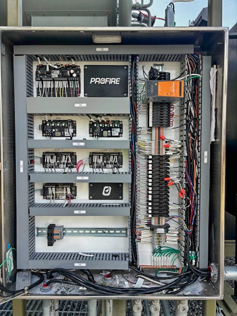 Open stainless-steel control panel showing neatly organized wiring, terminal blocks, relays, and Profire-branded control modules mounted on backplates and DIN rail.
