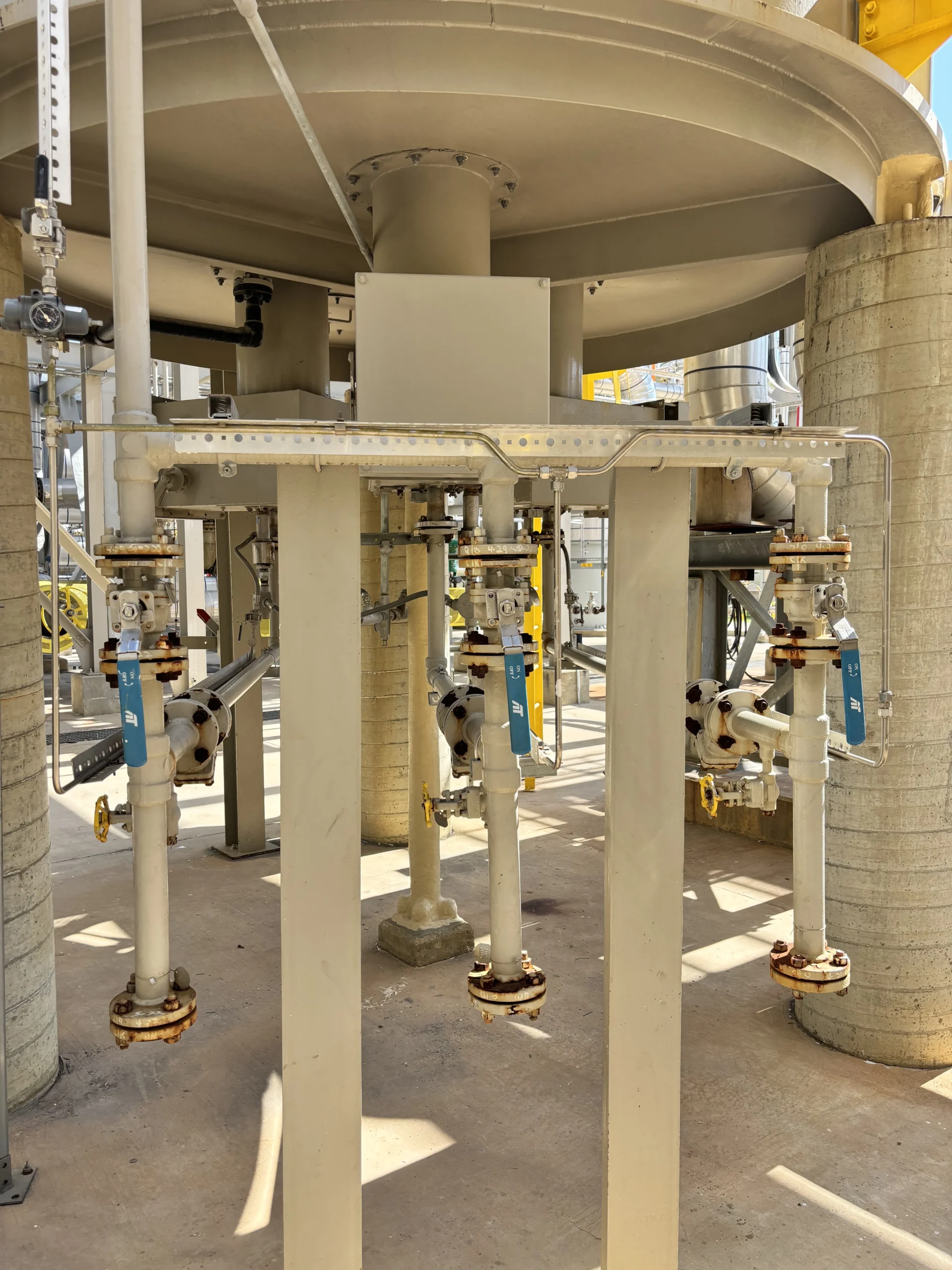 Underside view of an industrial process heater with three vertical burner fuel lines, blue-handled shutoff valves, and structural supports.