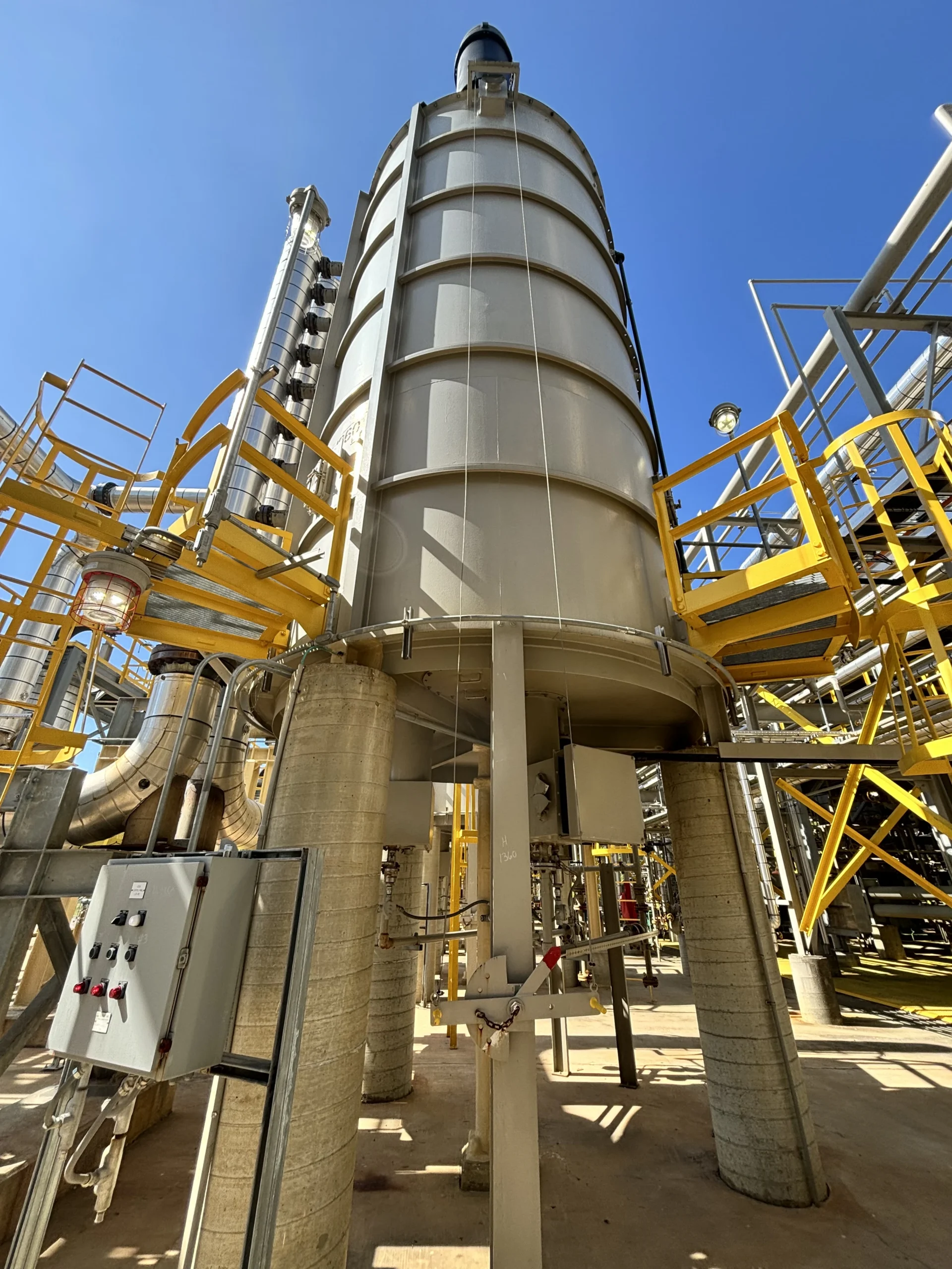 Wide view of a large vertical industrial process heater with yellow access platforms, piping, burner equipment, and a local control panel at the base.