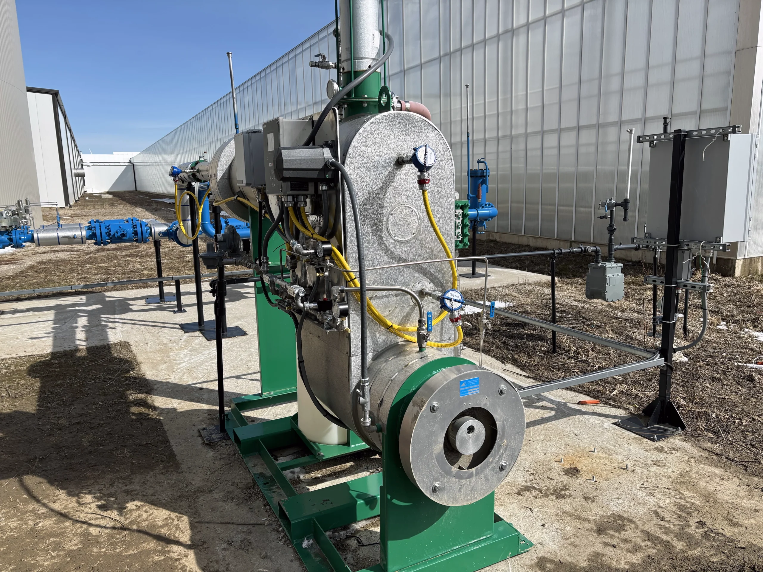 Skid-mounted fired heater with an insulated housing, burner assembly, instrumentation, and controls installed beside a greenhouse.