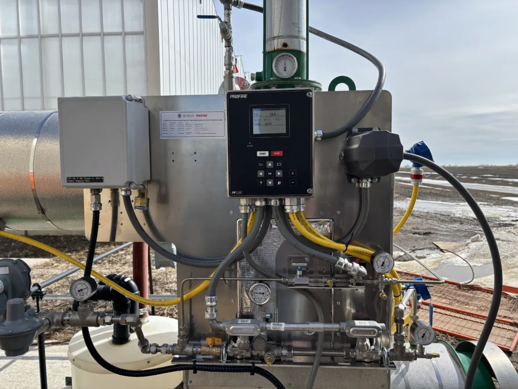 Close-up of a Profire PF2200 burner management controller, fuel train, pressure gauges, valves, and tubing on the heater skid.