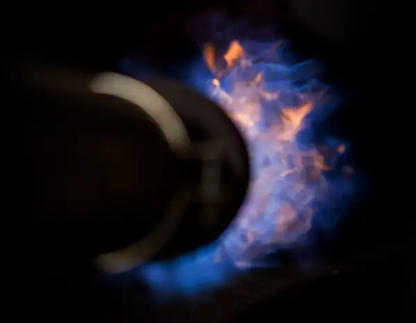 Close-up of a burner nozzle producing a blue and orange flame against a black background.