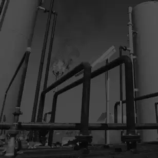 Dark, low-contrast photo of storage tanks and connecting pipework at a gas processing facility.