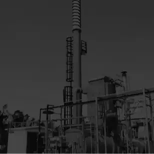 Dark, low-angle photo of tall cylindrical industrial vessels and connecting pipes.