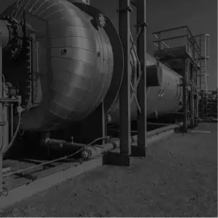 Dark, low-contrast photo of an industrial processing plant with piping, stacks and structural steel.
