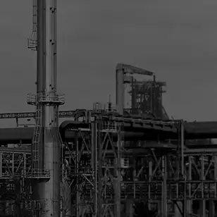 Dark, low-contrast photo of tall industrial processing structures and piping against a gray sky.