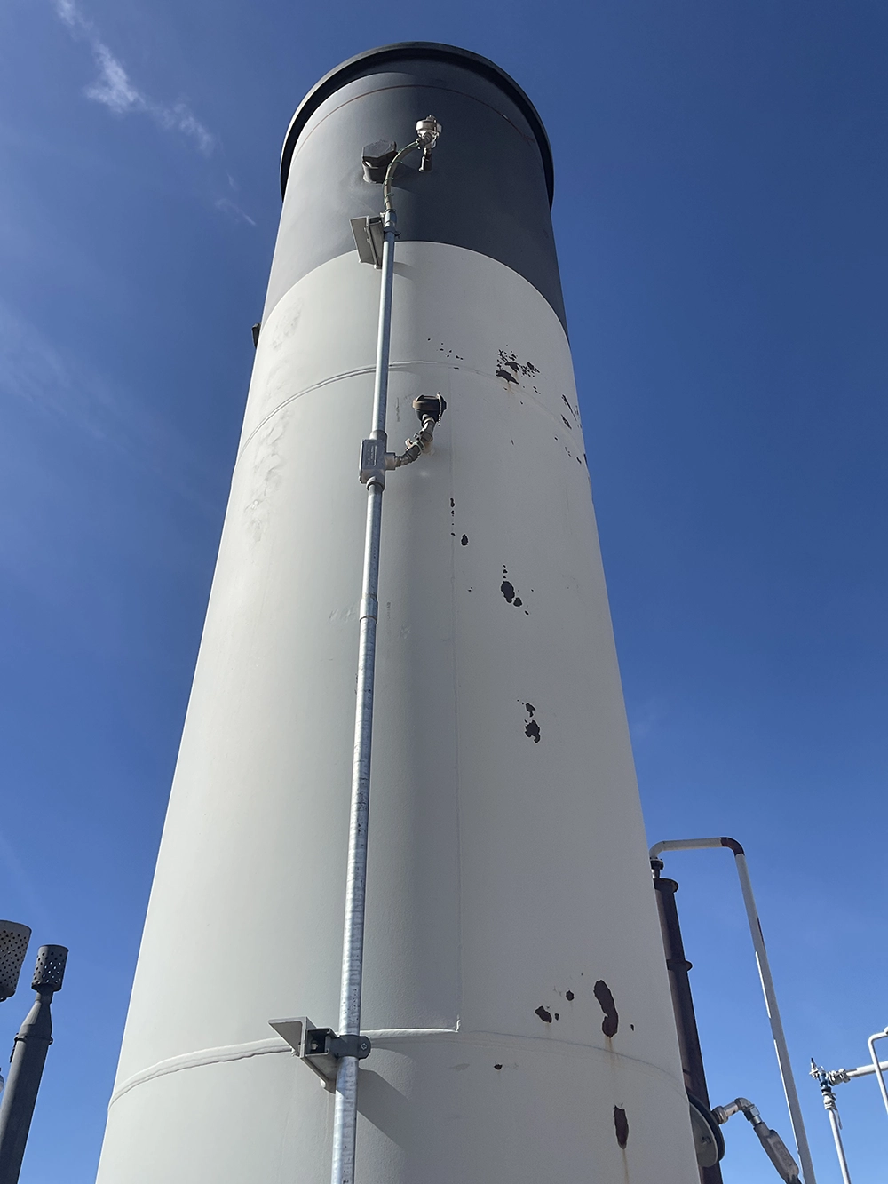 Upward view of a cylindrical incinerator stack equipped with external instrumentation.