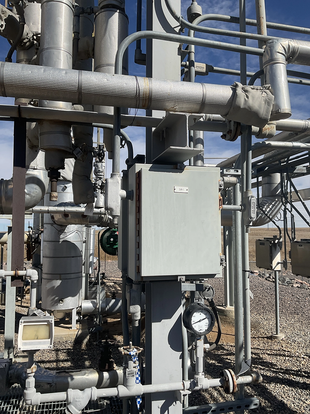 Control enclosure and pressure gauge installed among insulated piping on a TEG reboiler and incinerator system.